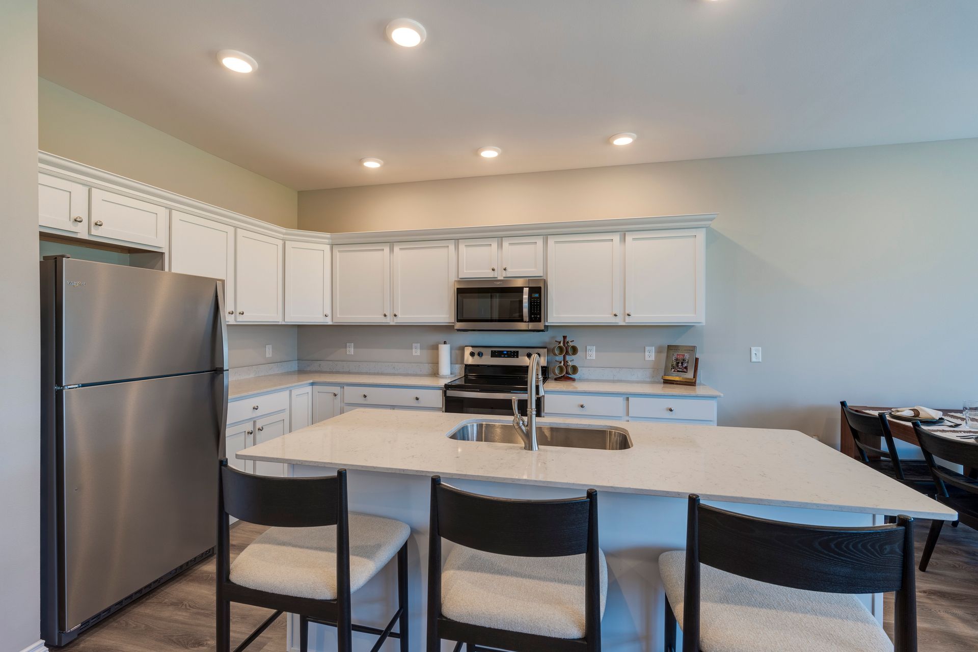 Modern kitchen with white cabinets, stainless steel appliances, and a large island with black stools.