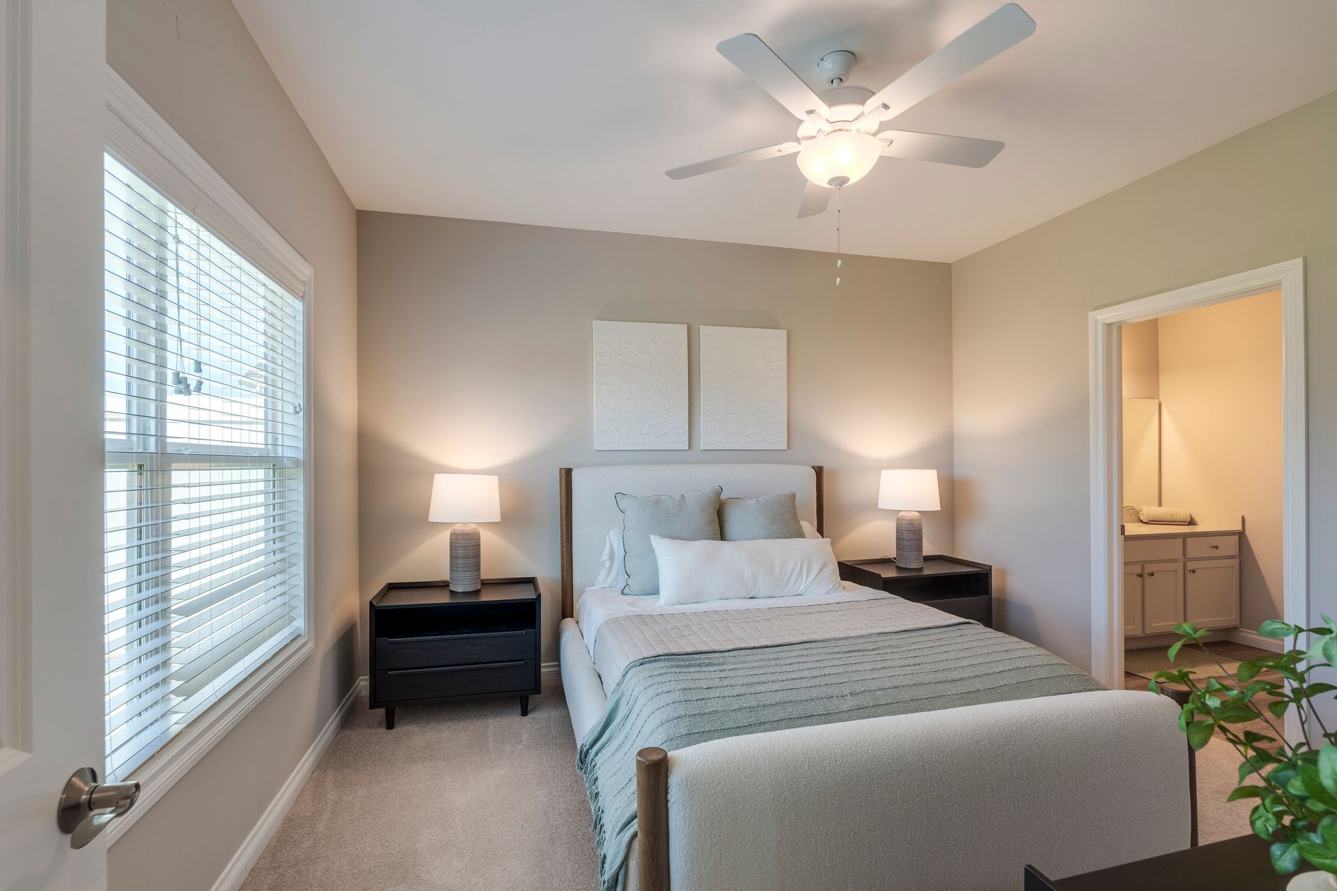 Bedroom with a bed, nightstands, lamps, window with blinds, and a doorway to a bathroom.