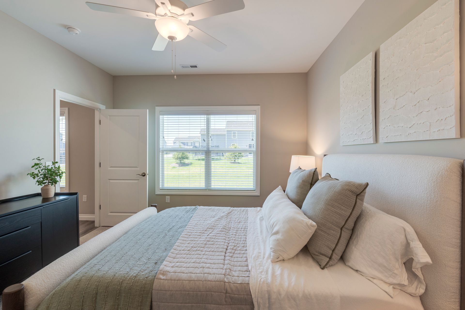 Bedroom with a bed, dresser, window, and decorative art. Soft neutral tones.