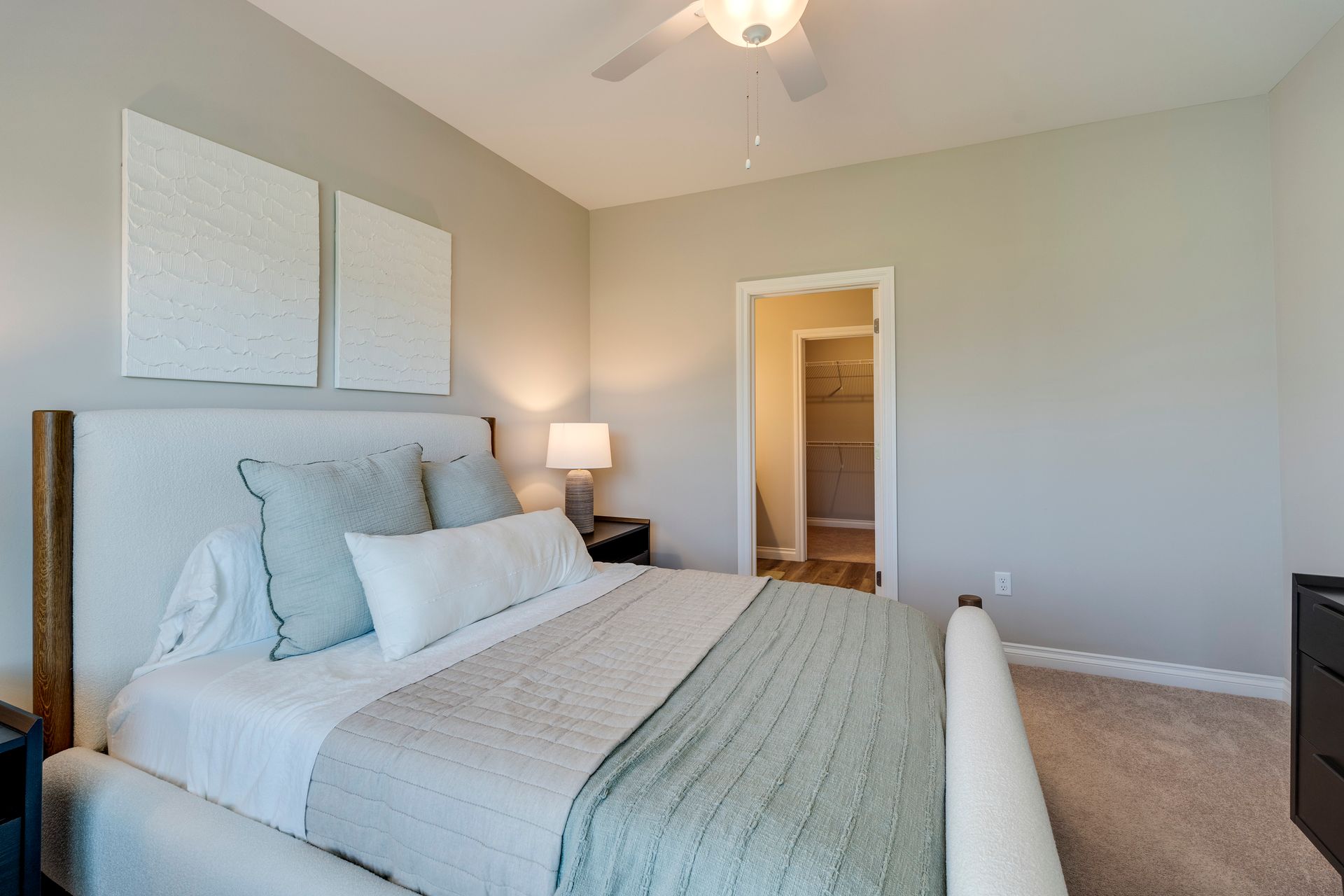 Bedroom with bed, pillows, blanket, art, nightstand, and closet.
