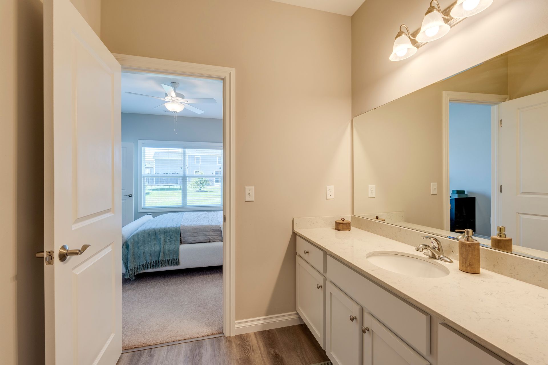 Bathroom with a vanity and a doorway to a bedroom with a bed and window.