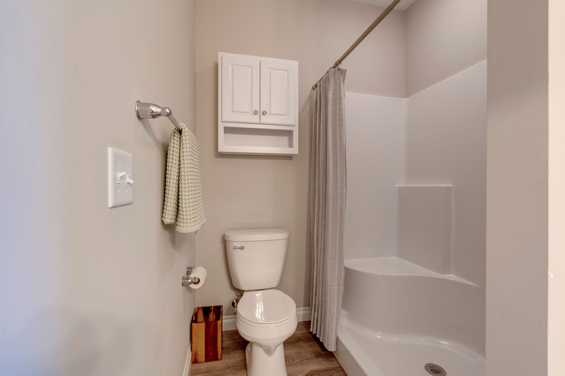 Small, white bathroom with shower, toilet, and cabinet on a beige wall.