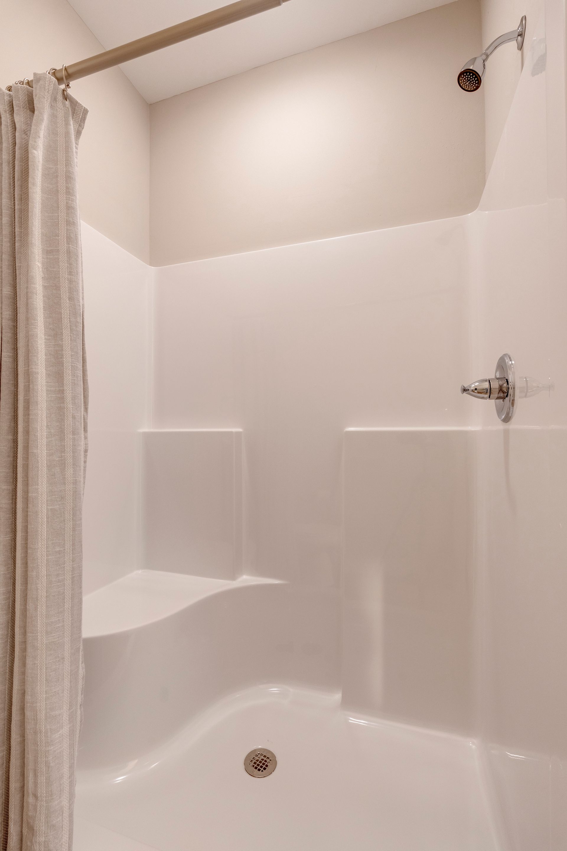 White-walled shower with built-in seat and showerhead; curtain partially drawn.