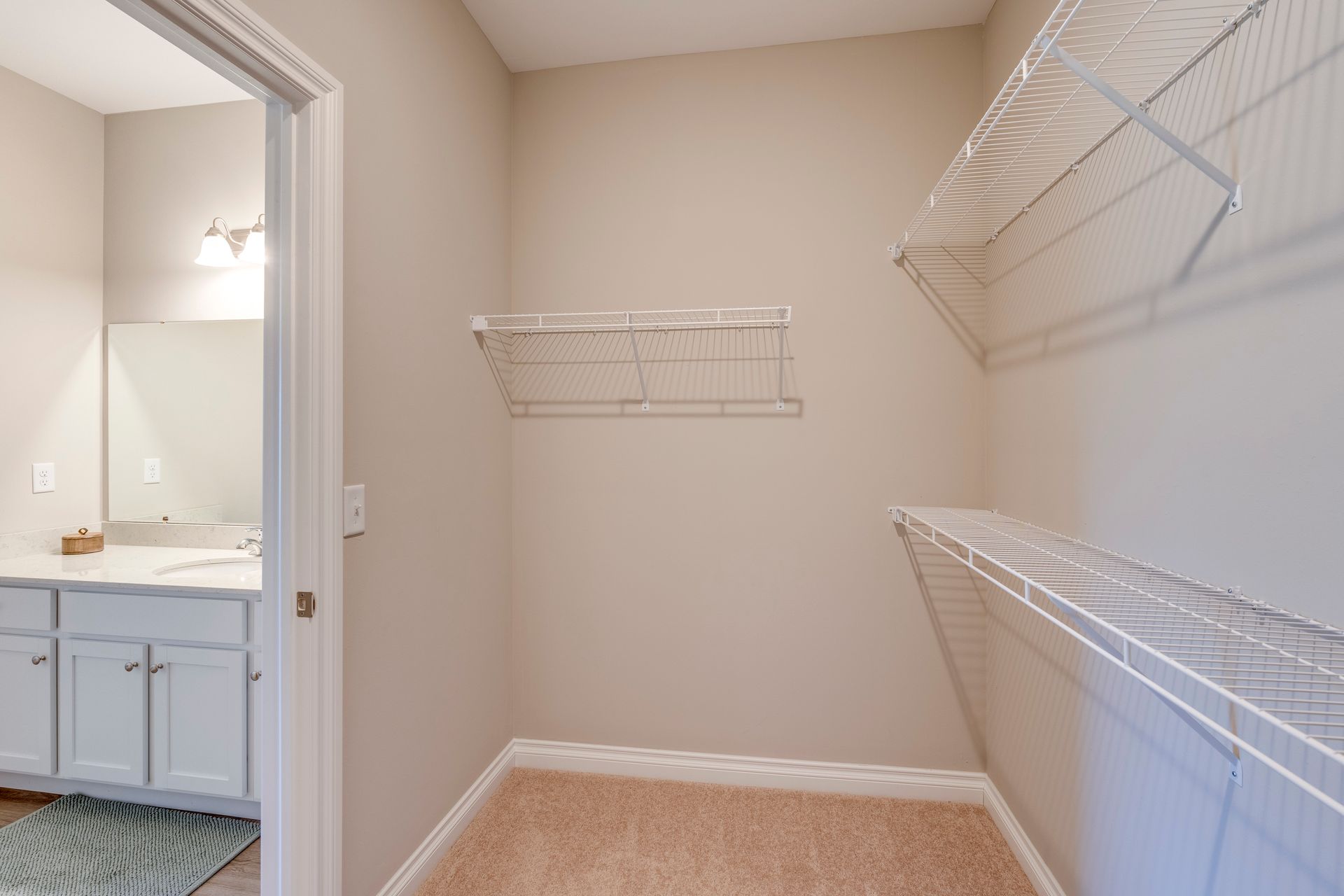 Empty walk-in closet with wire shelving and doorway to a bathroom with a white vanity.