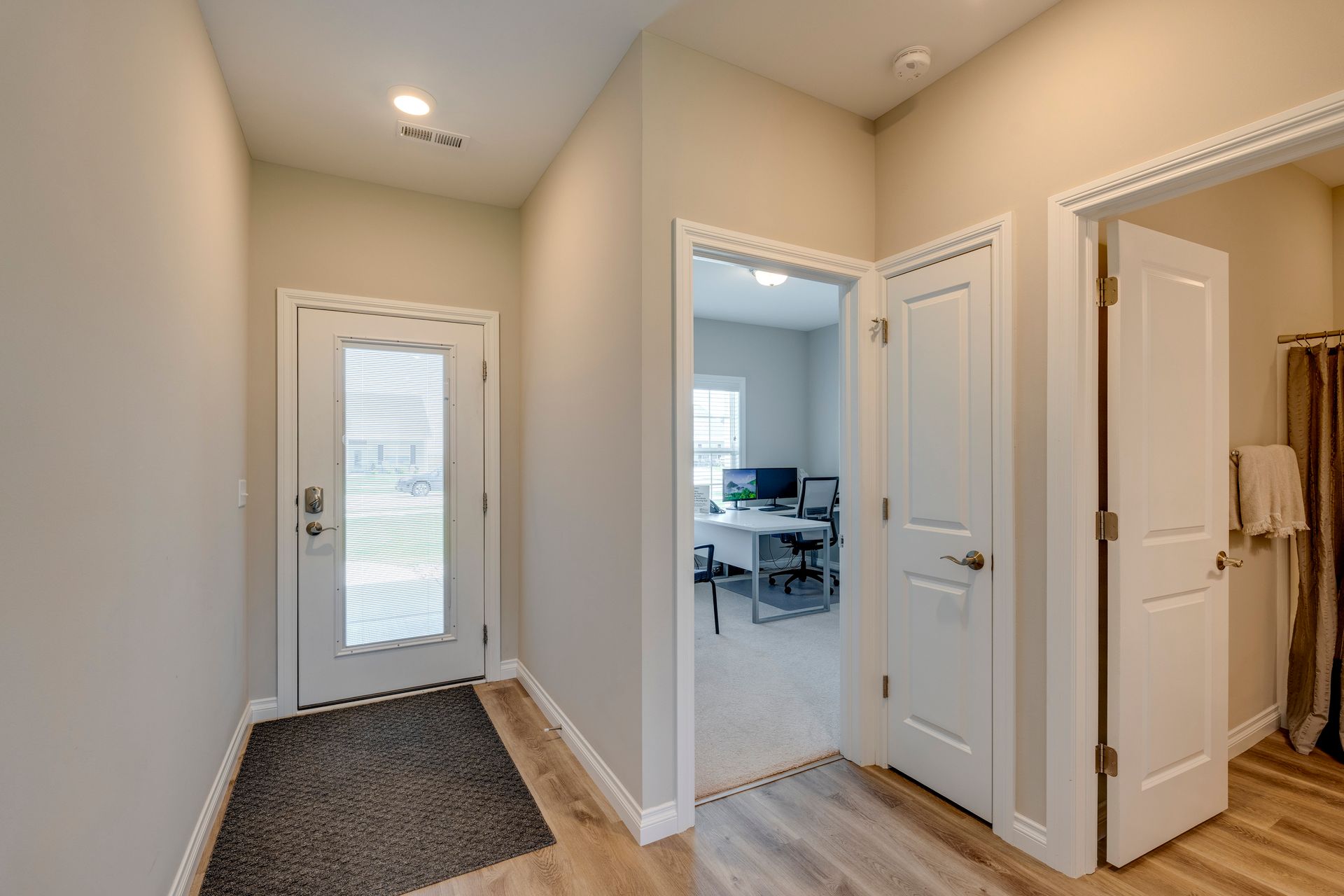 Entryway with front door, office, and bathroom doors. Light walls and wood-look flooring.