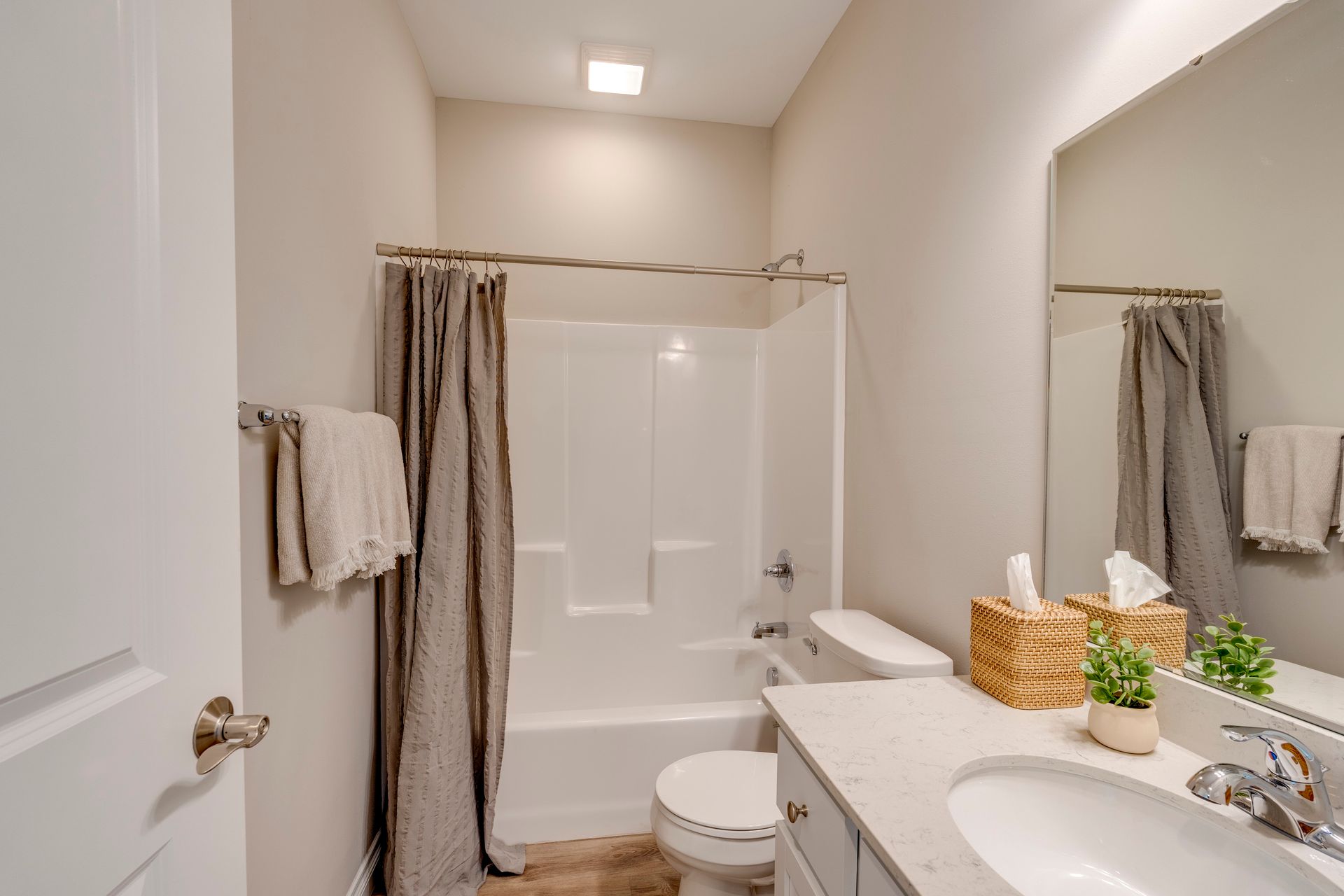 Bathroom with shower, toilet, sink, mirror, and towels. Neutral color scheme, simple décor.