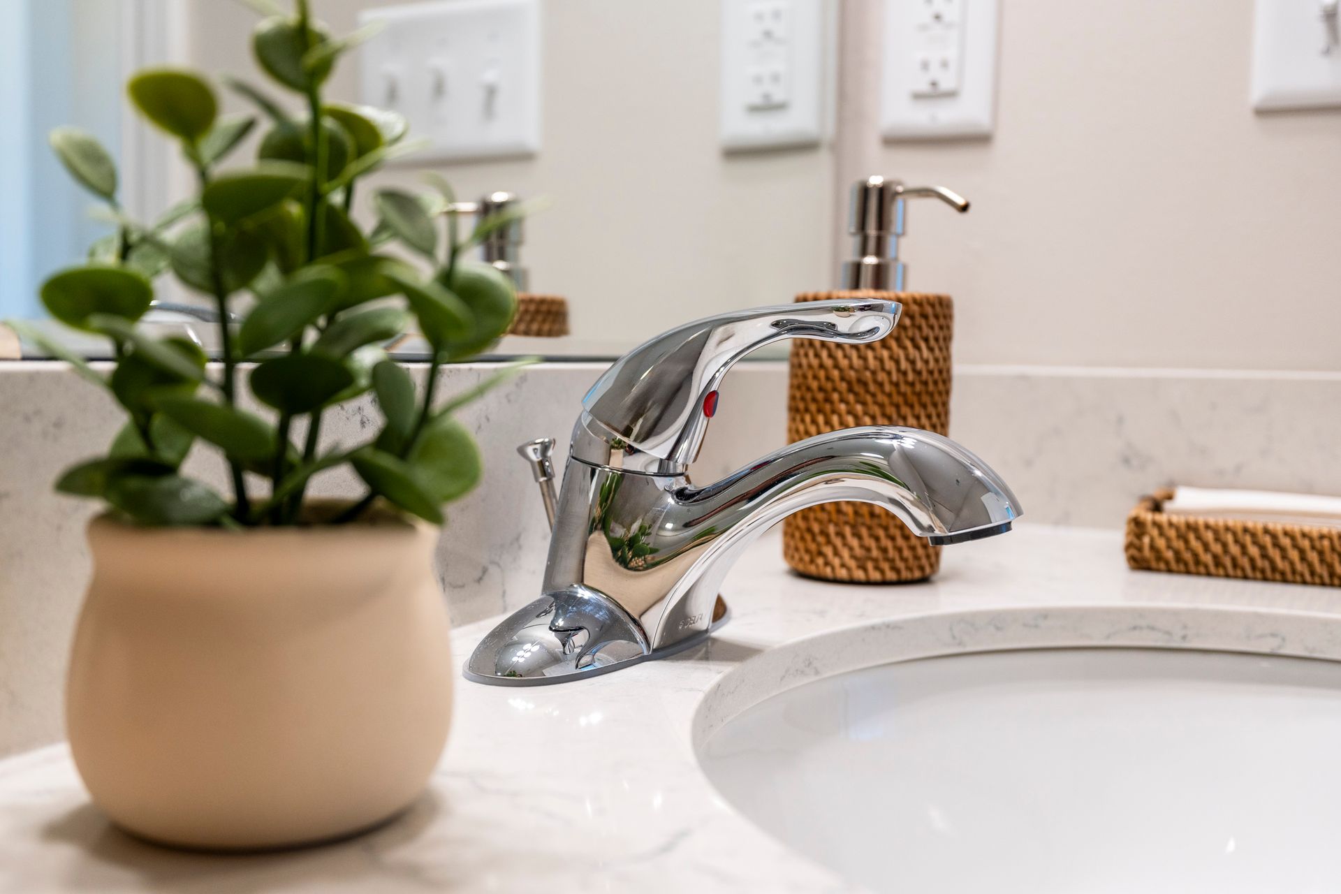Close-up of a bathroom sink with chrome faucet, potted plant, and soap dispenser on a marble countertop.