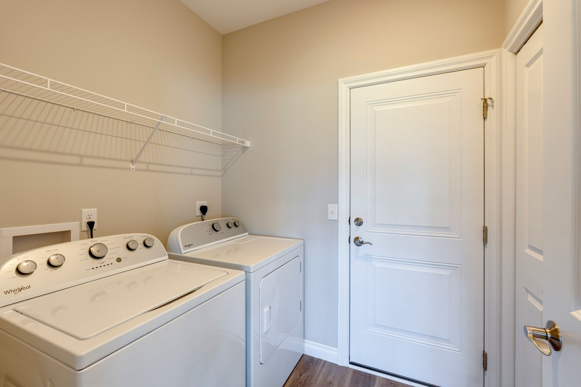 Laundry room with a washing machine and dryer, wire shelf, and a white door.