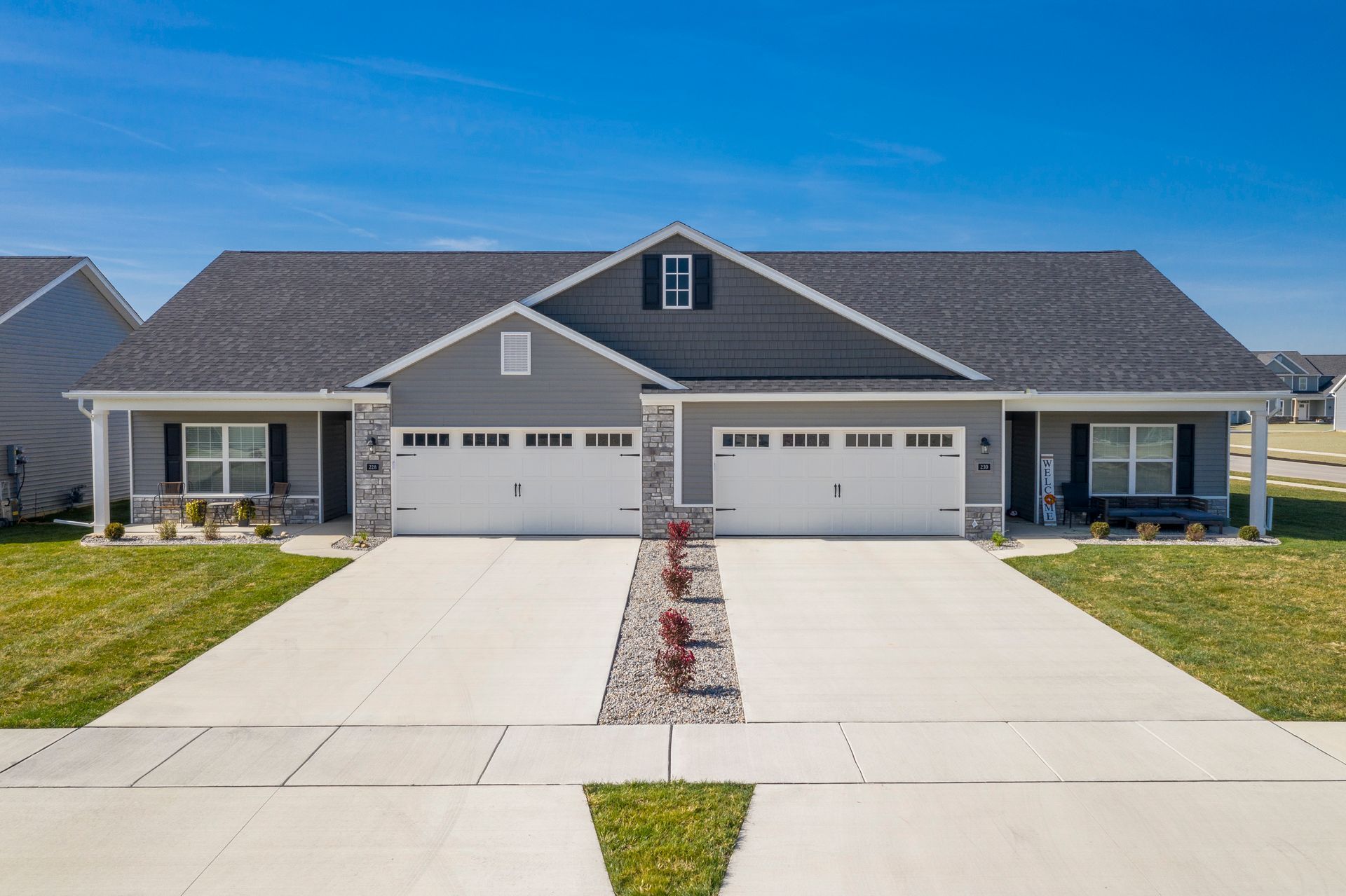 Duplex with gray siding, two-car garages, and a small front yard with a flower bed. Sunny day.