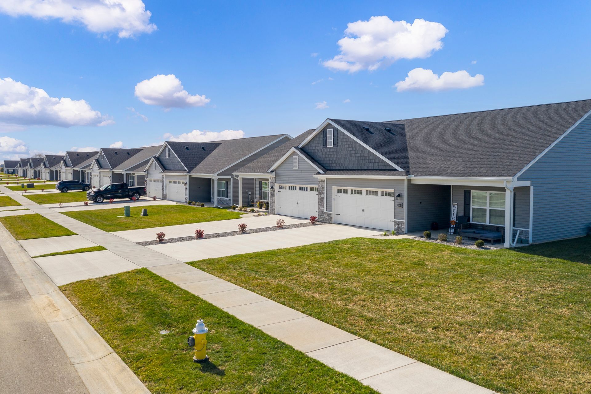 Row of gray houses with white garage doors and green lawns on a sunny day.