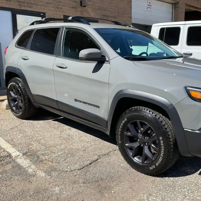 Gray Jeep Cherokee SUV with black wheels parked outdoors on concrete.