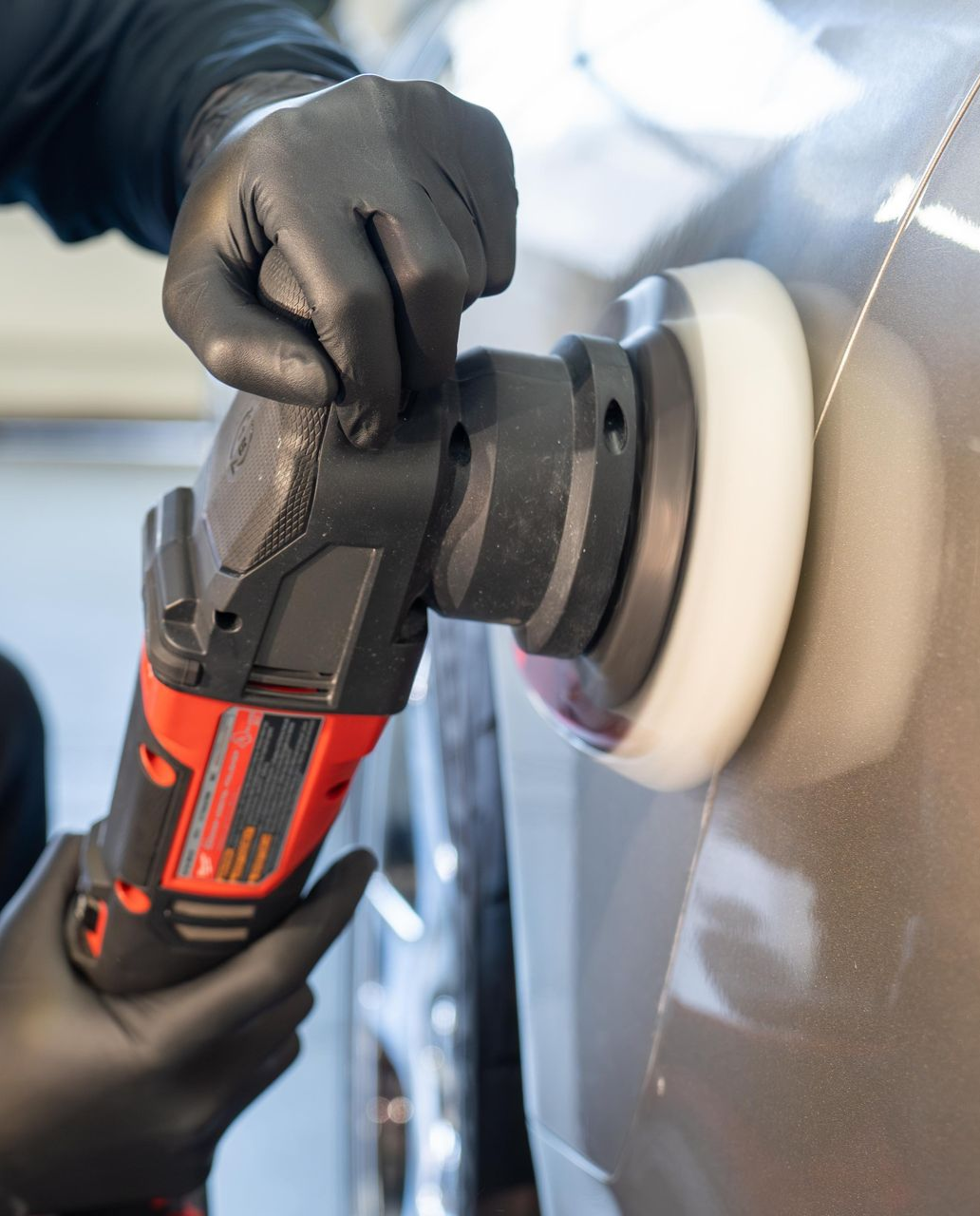 Hands wearing black gloves using a red and black polisher on a car's paint.