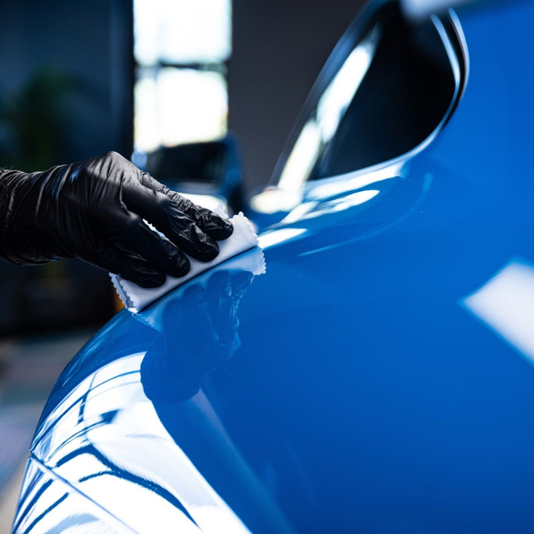 Hand using an electric polisher with a yellow buffing pad on a vehicle's surface.