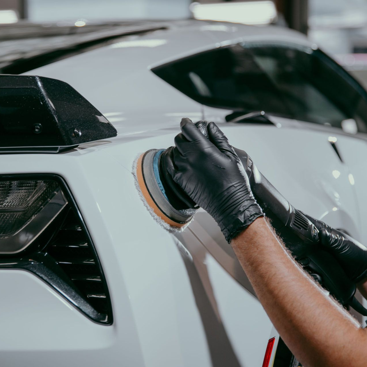 Person wearing black gloves polishing a white sports car's rear.