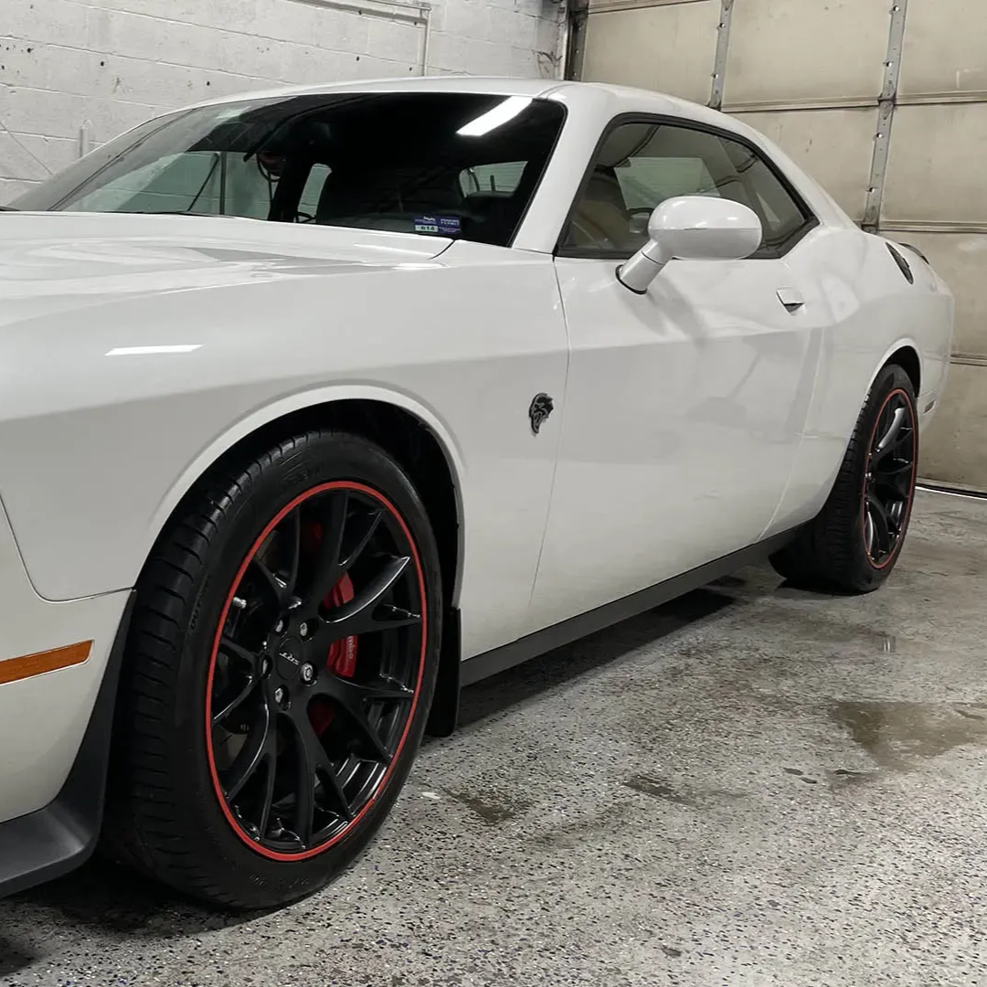 White Dodge Challenger sports car with black wheels and red accents in a garage.
