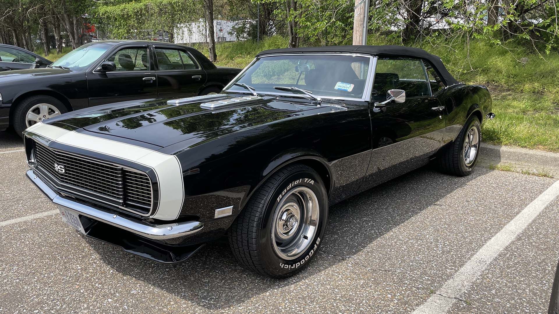 Black vintage Chevrolet Camaro with white racing stripes parked in a lot.