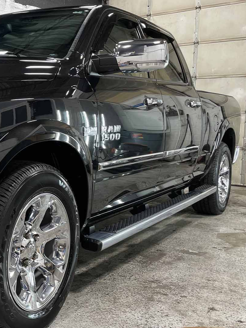 Black Ram 1500 truck with chrome accents parked in front of a light-colored wall.