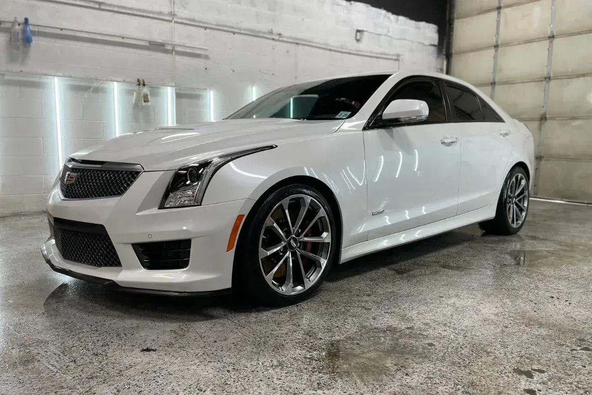 White Cadillac sedan parked indoors, glossy finish, black accents, gray wheels.