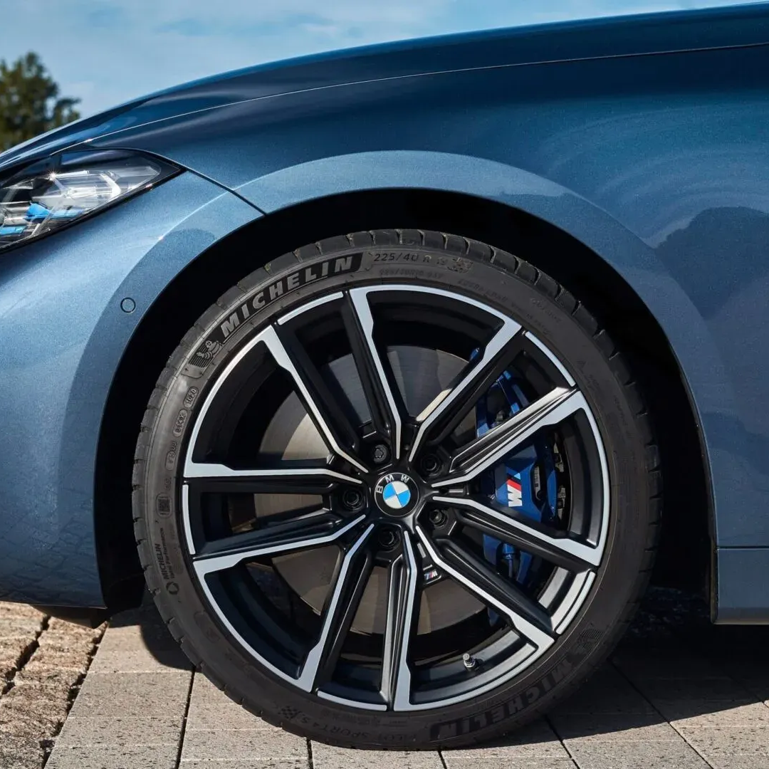 Blue BMW car wheel, black and silver rim, blue brake caliper, Michelin tire on a brick surface.