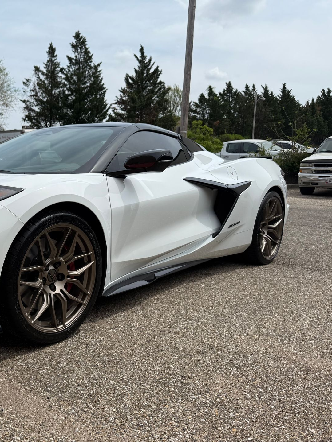 White Corvette sports car with bronze wheels parked on gravel. Black roof and side accents.