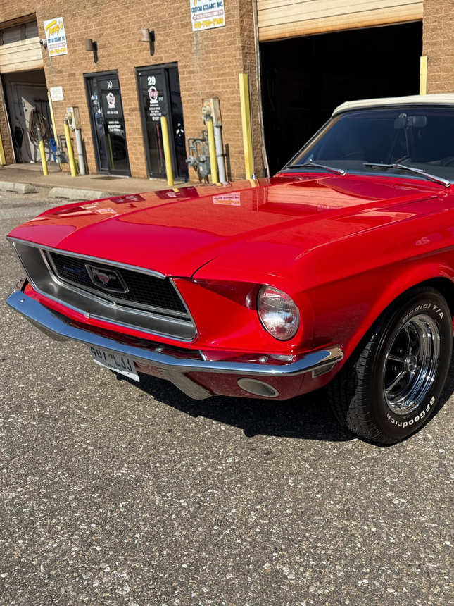 Red 1967 Ford Mustang convertible parked in front of a brick building with black doors.
