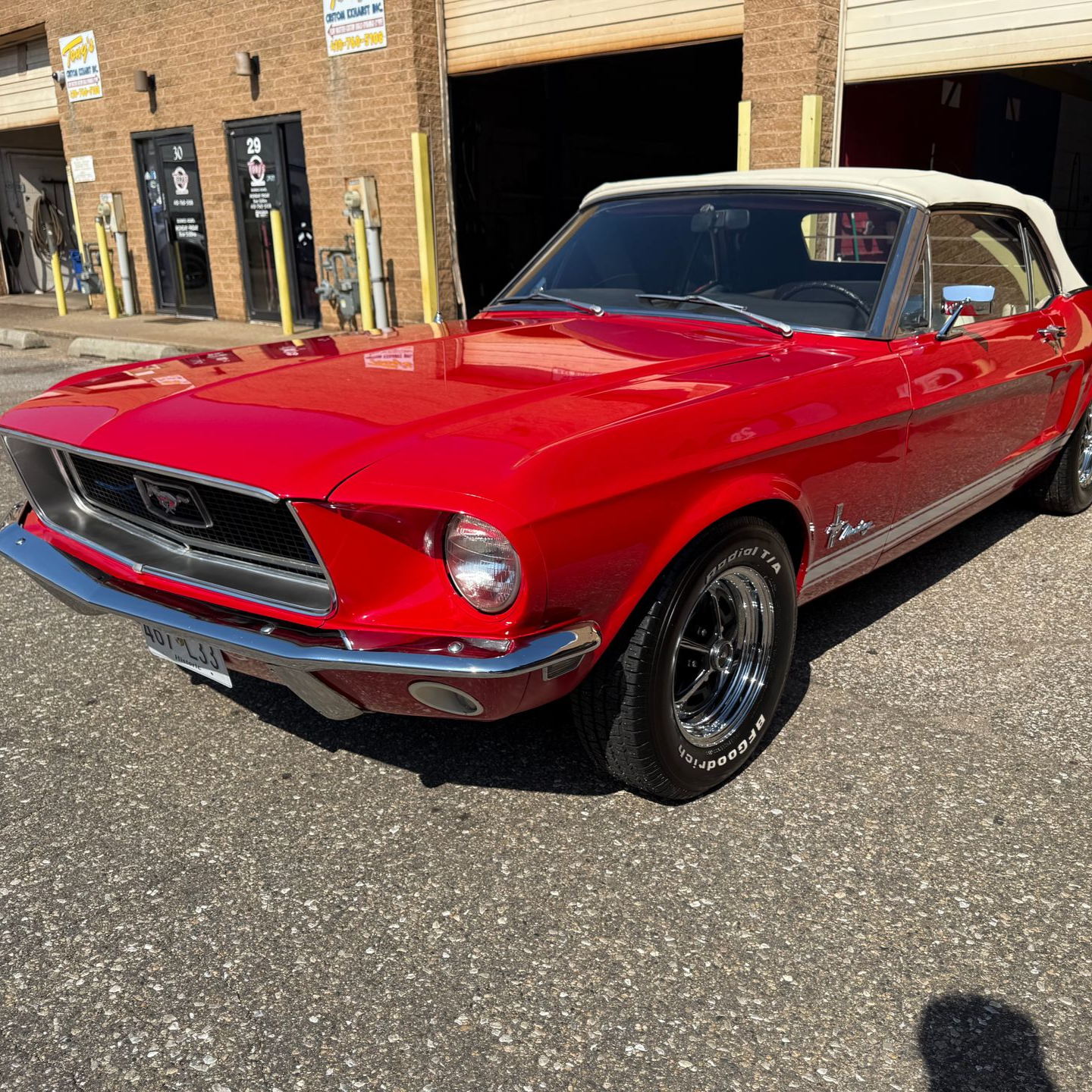 Red 1967 Ford Mustang convertible parked in front of a garage with a white top and chrome accents.