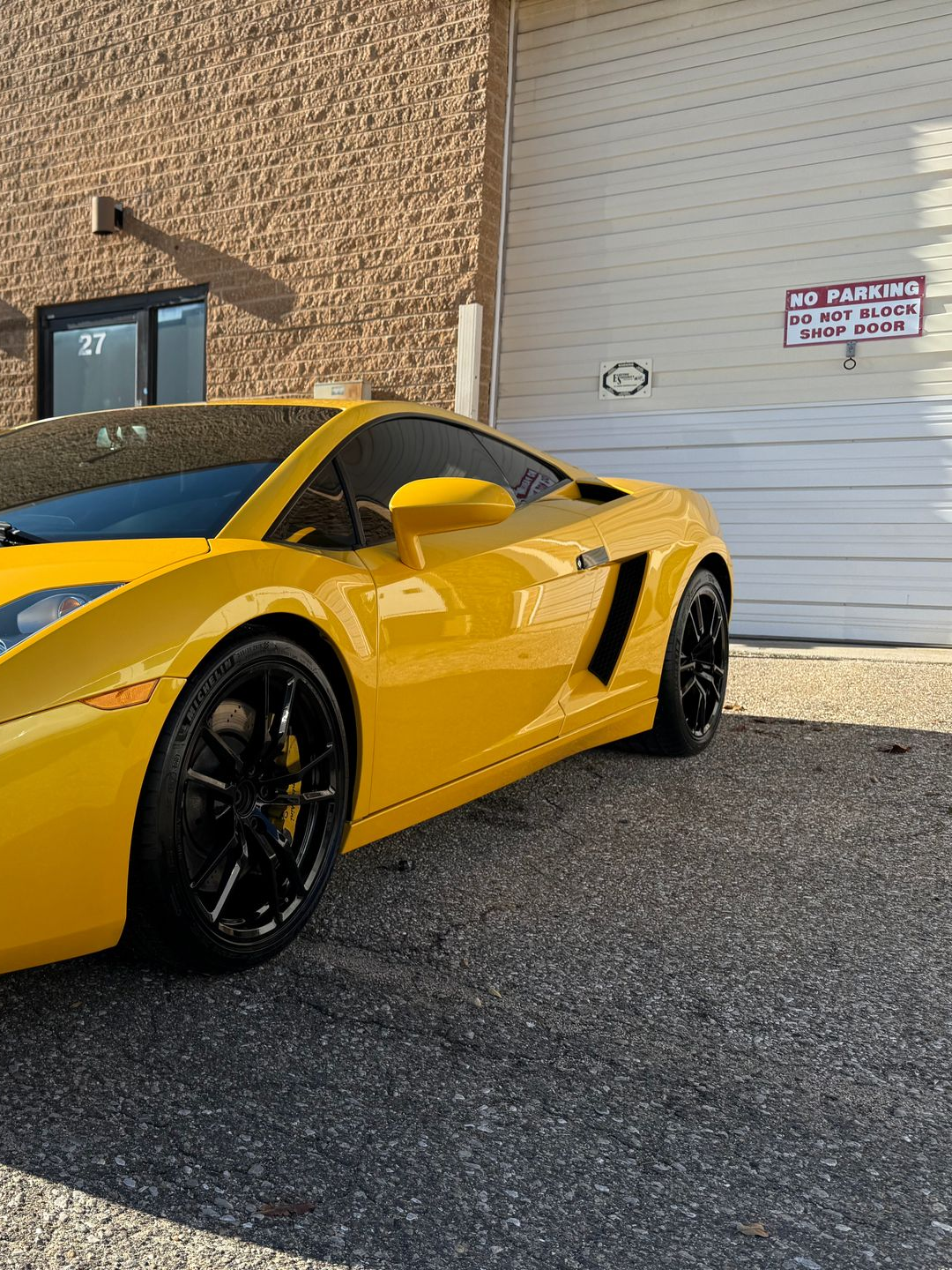 Yellow Lamborghini parked in front of a building with a garage door, black wheels and tinted windows.