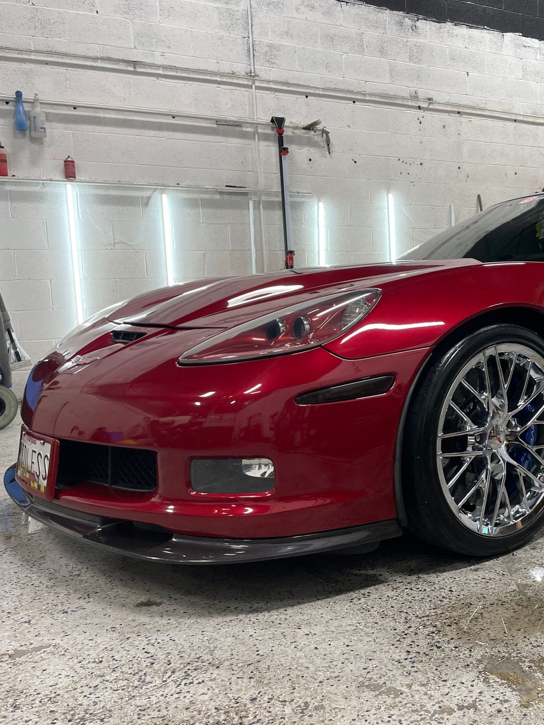 Red Corvette sports car with chrome wheels, inside a well-lit garage.