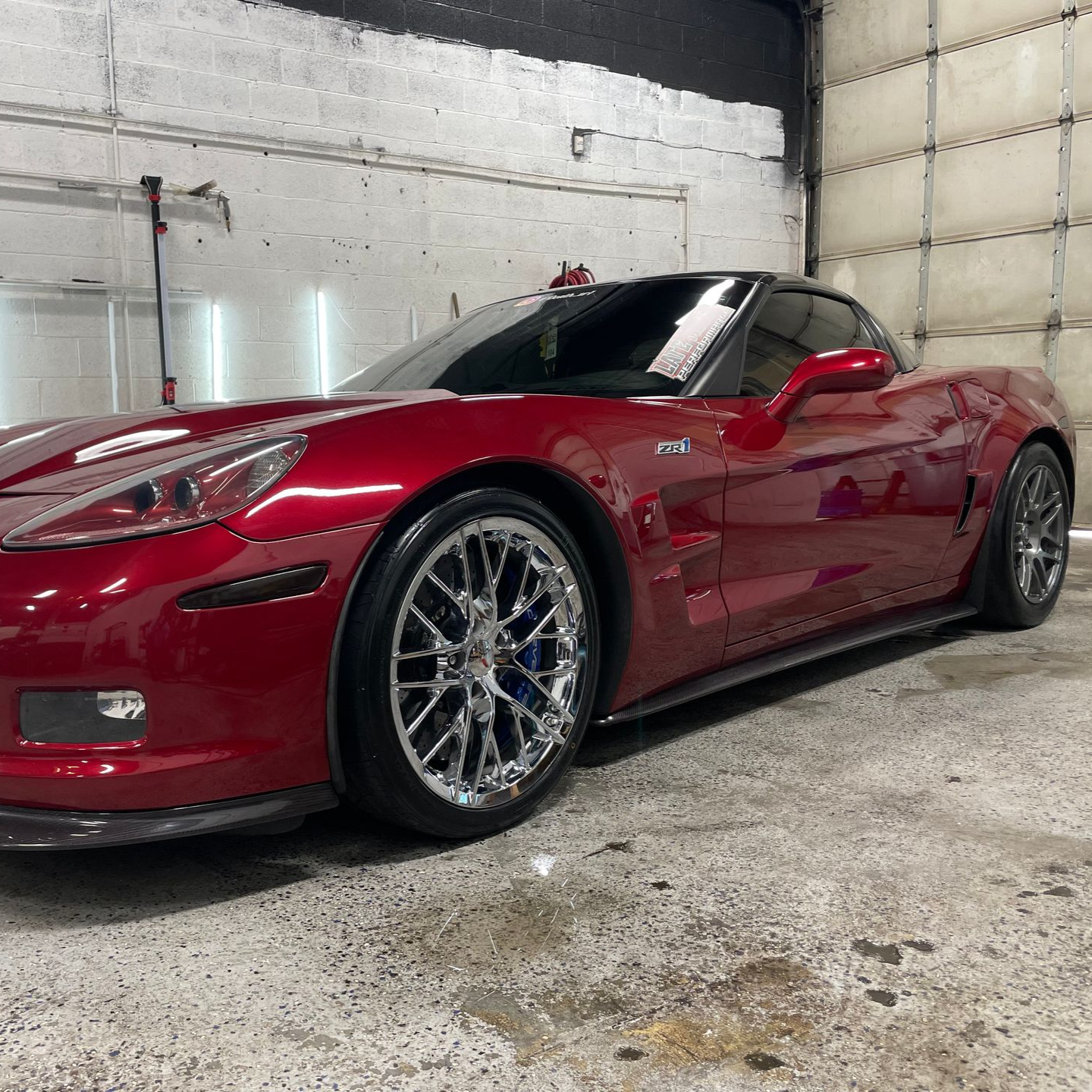 Red Corvette sports car with chrome wheels in a garage.
