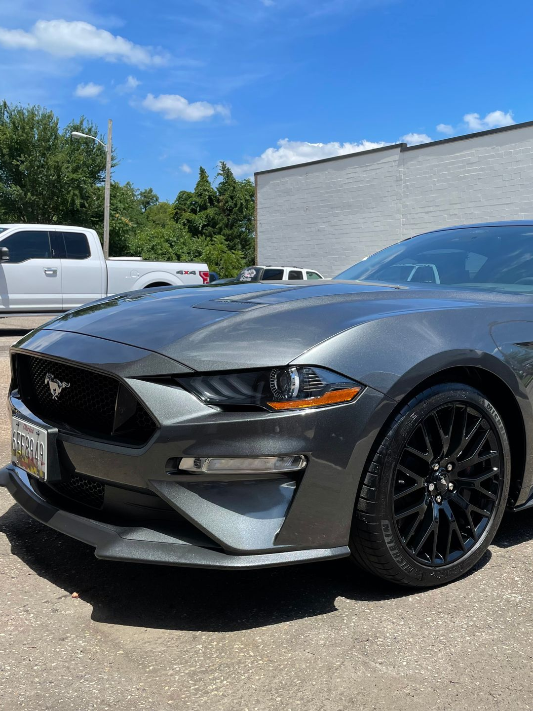 Gray Ford Mustang with black rims parked outside on a sunny day.