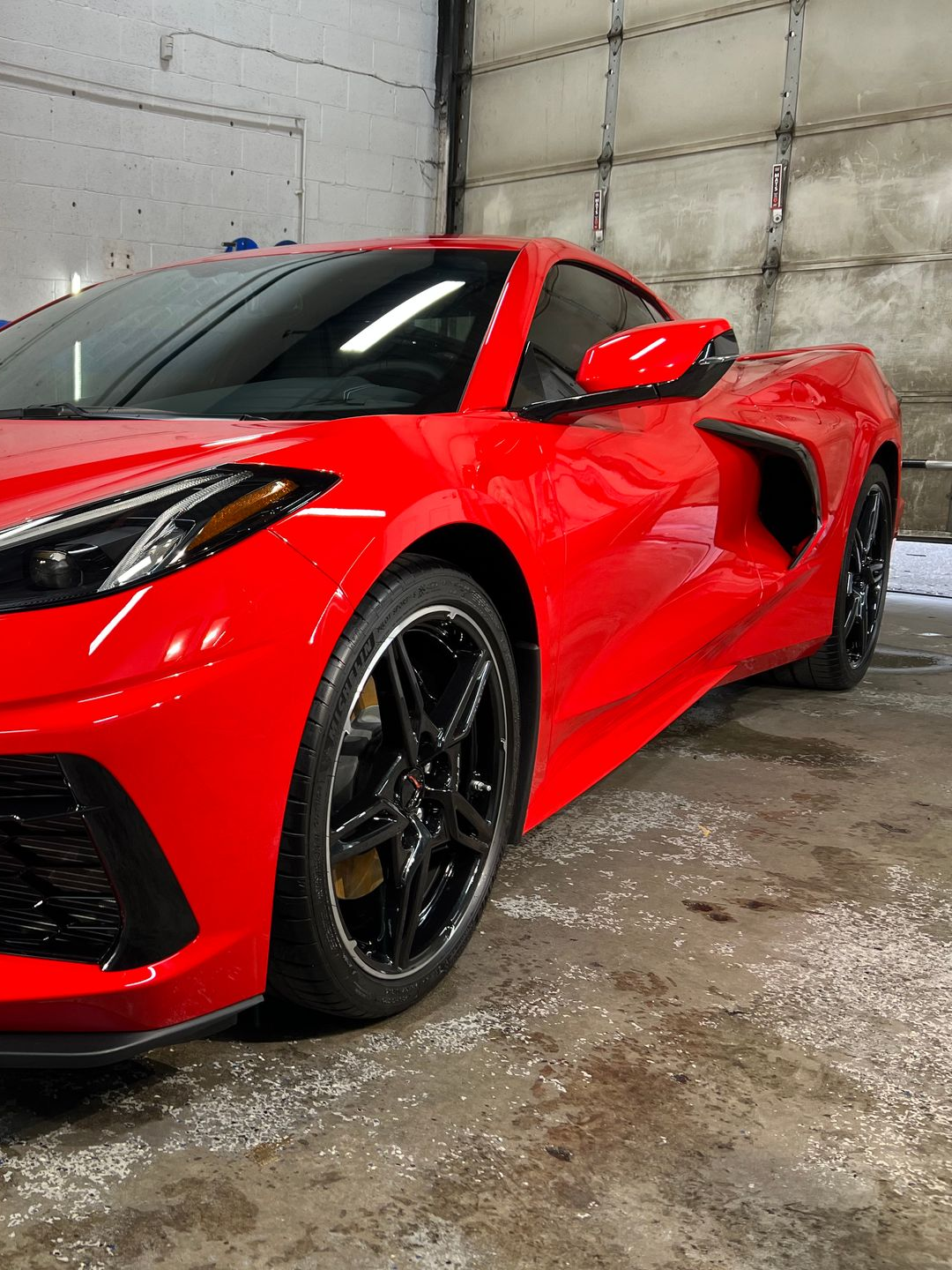 Red Chevrolet Corvette sports car parked inside a garage with a concrete floor.