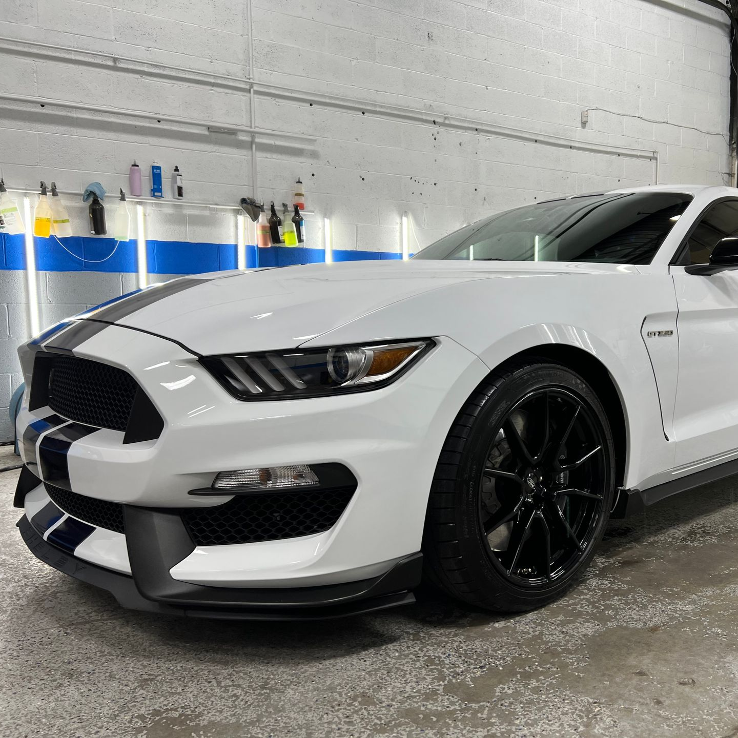 White Ford Mustang Shelby GT350 with black stripes, parked in a garage.