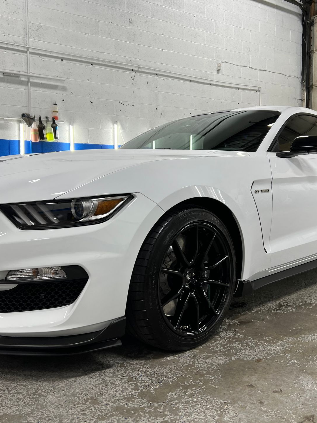 White Ford Mustang GT350 with black rims parked indoors.