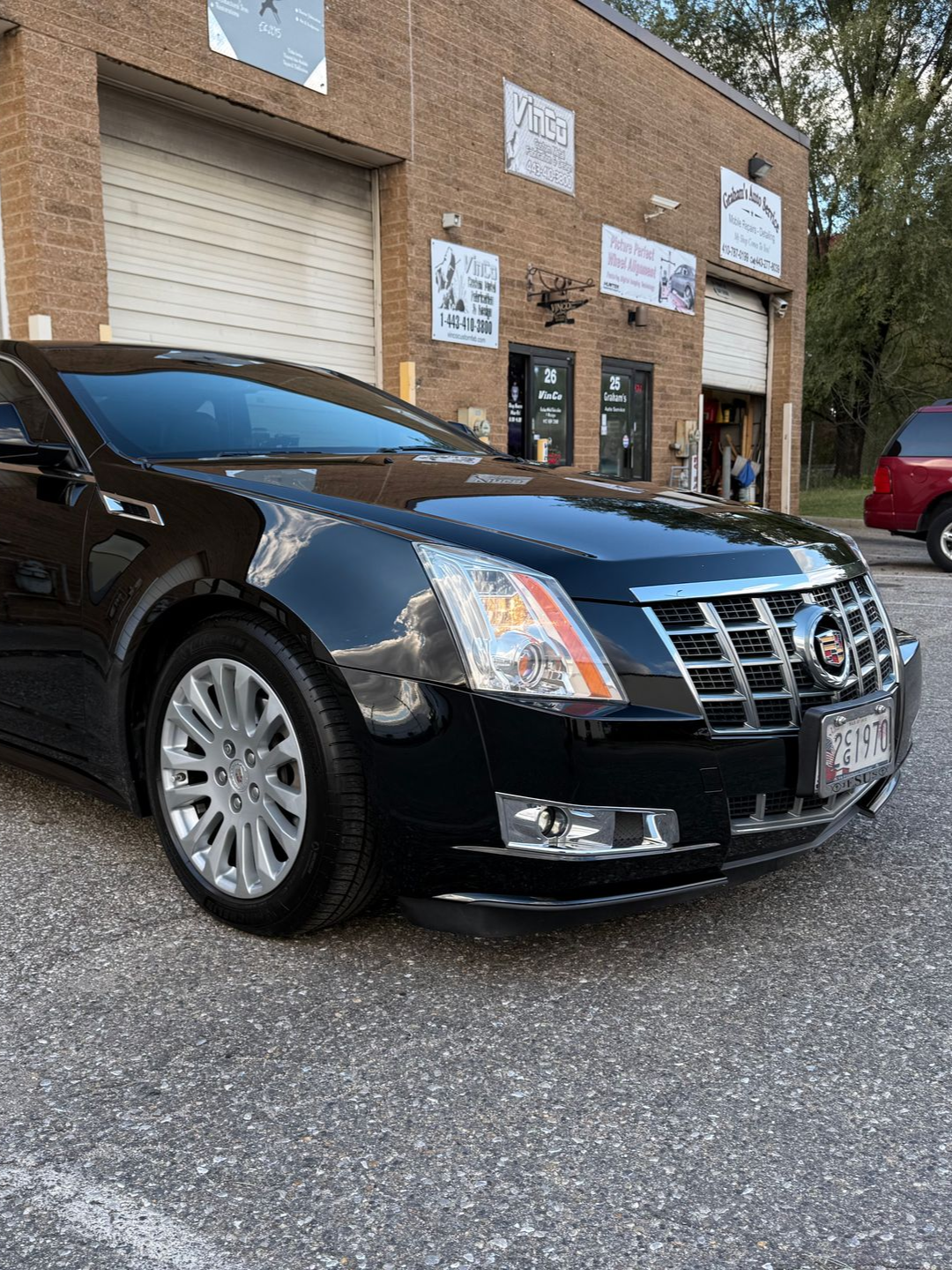 Black Cadillac in front of a brick building with garage doors; parked on a paved surface.