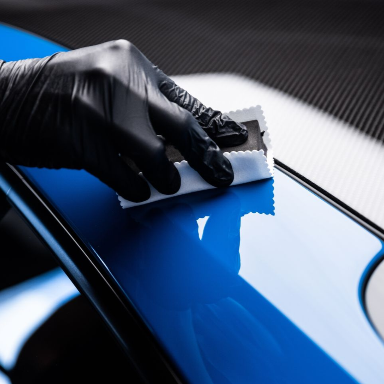 Gloved hand applying ceramic coating to a glossy blue car surface.