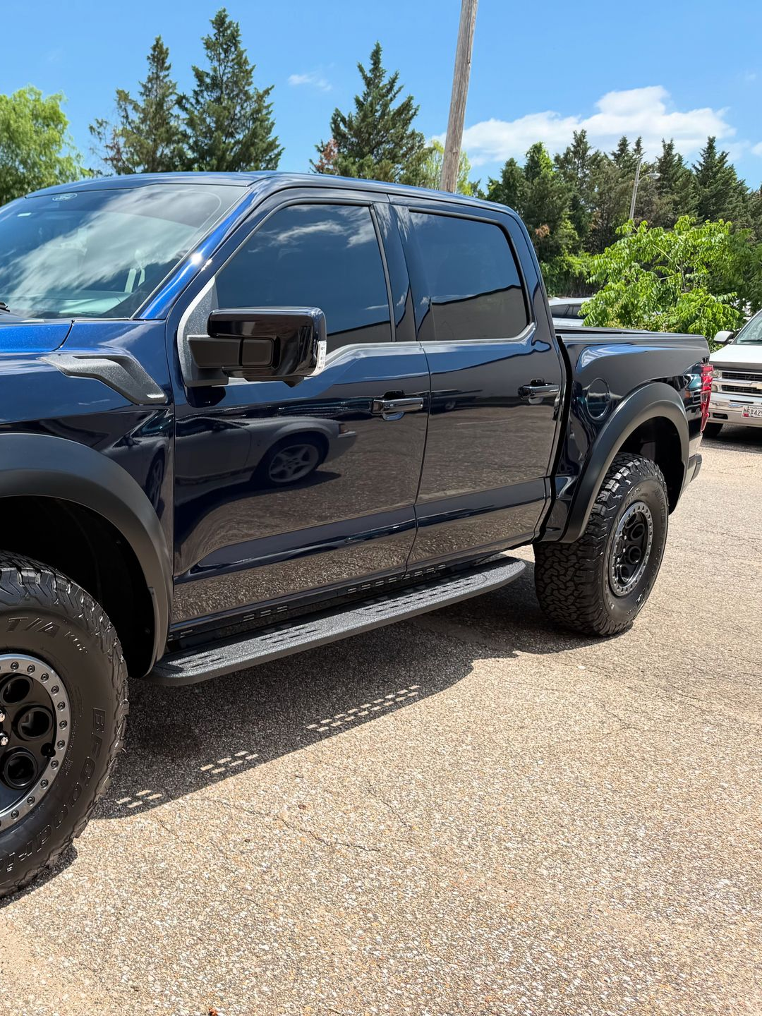 Dark blue Ford Raptor pickup truck parked on asphalt. Black accents, tinted windows, and trees in background.