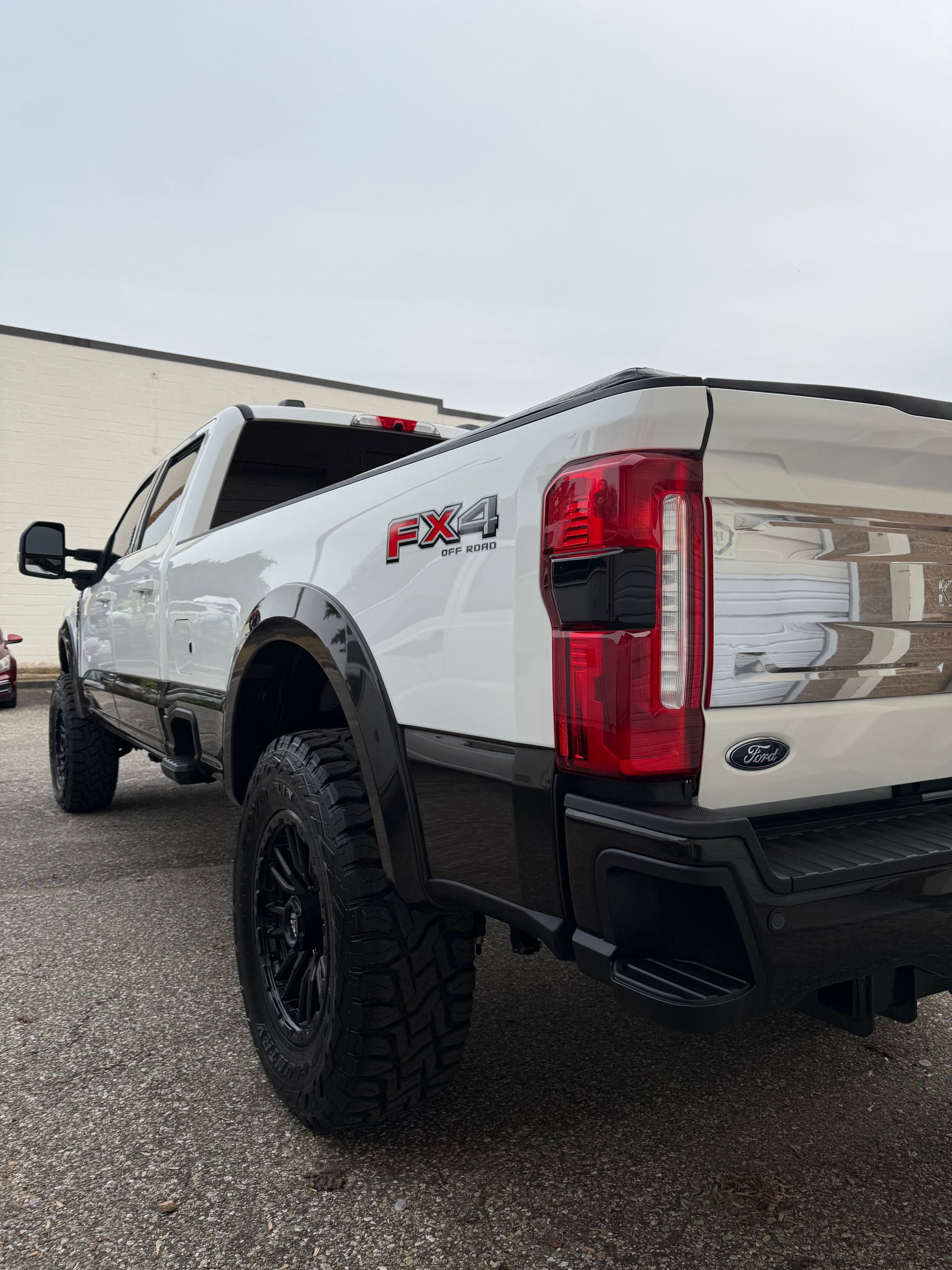 White and black Ford F-250 pickup truck, FX4, outdoors. Black wheels, tinted windows.