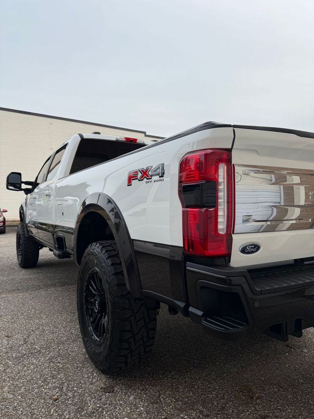 White and black Ford F-250 pickup truck, FX4, outdoors. Black wheels, tinted windows.