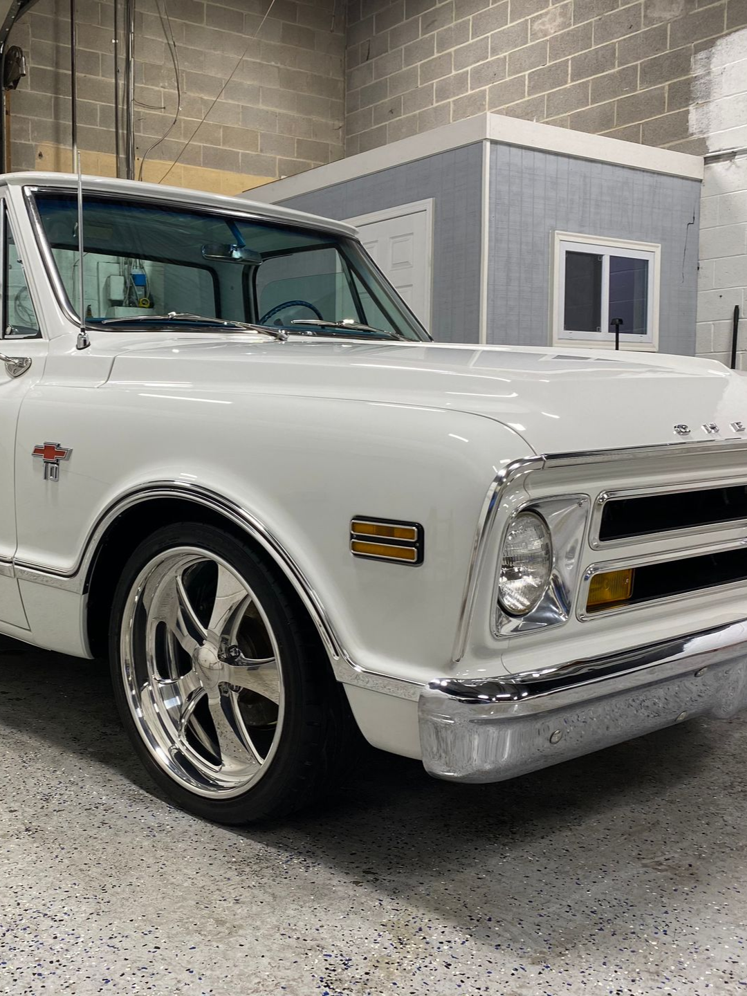 White 1968 Chevrolet C10 truck with chrome accents, shiny wheels, in a garage.