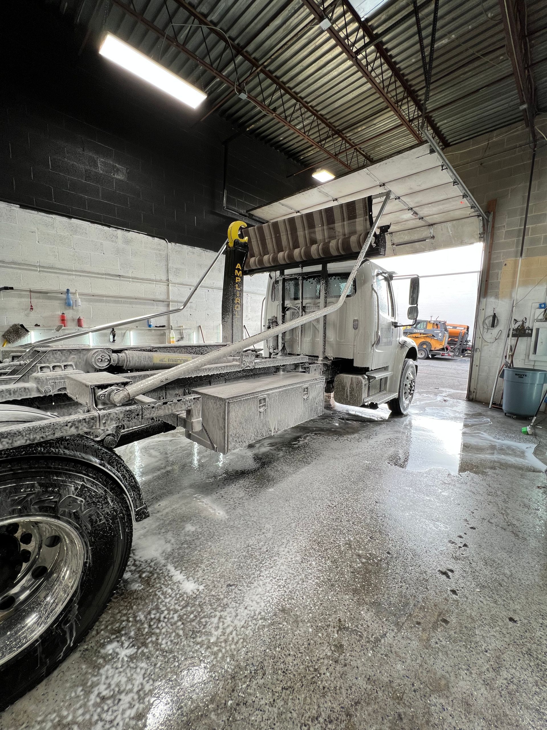A large truck being washed with soap in a warehouse. Foam covers the vehicle and floor.