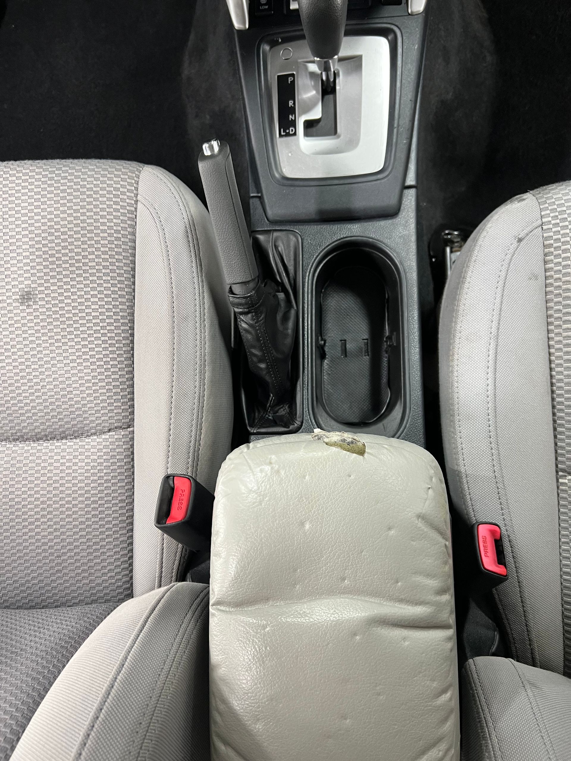 Car interior: center console with automatic gear shift, cup holder, parking brake, and armrest. Seats visible.