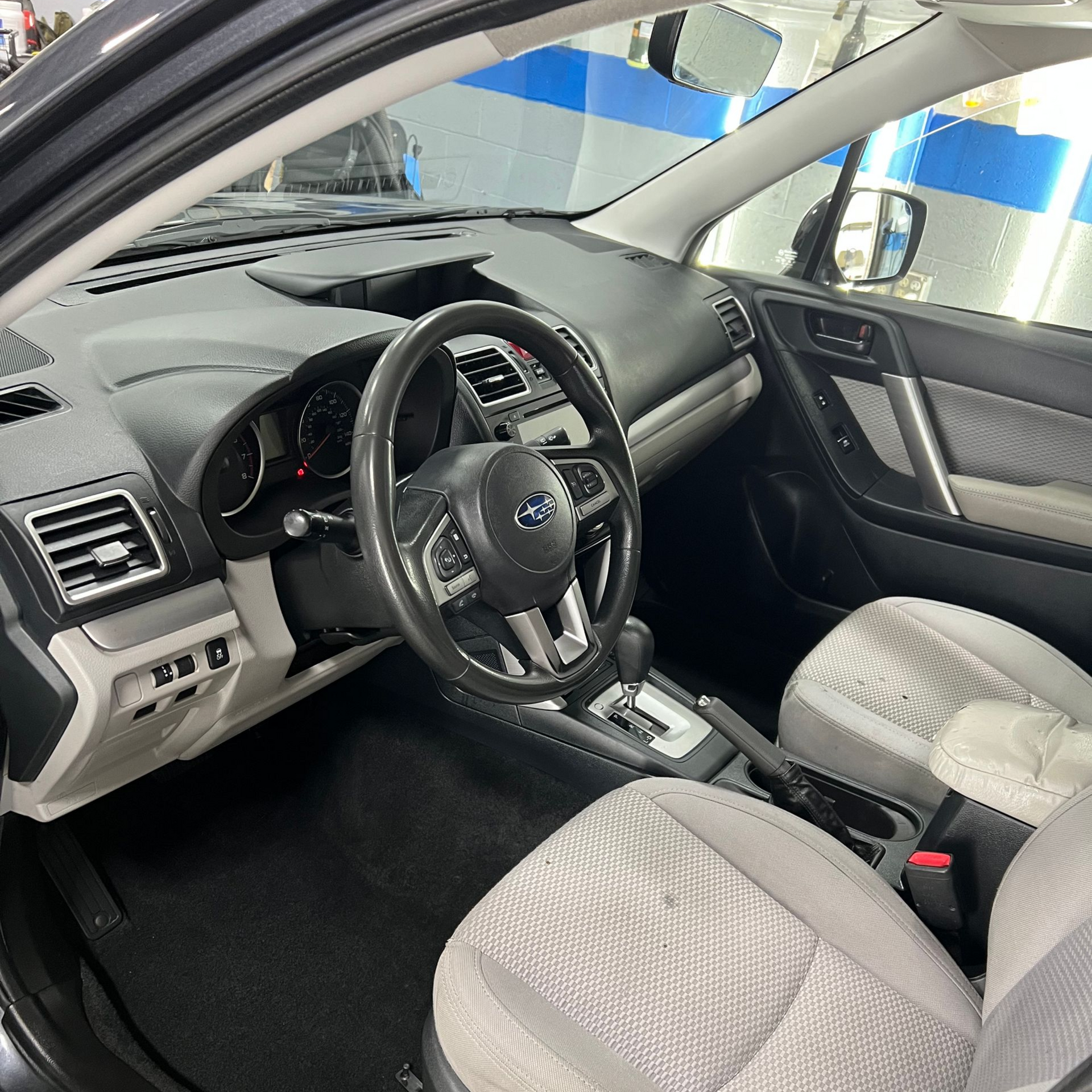 Interior of a Subaru Forester: black dashboard, gray seats, black steering wheel, silver accents.