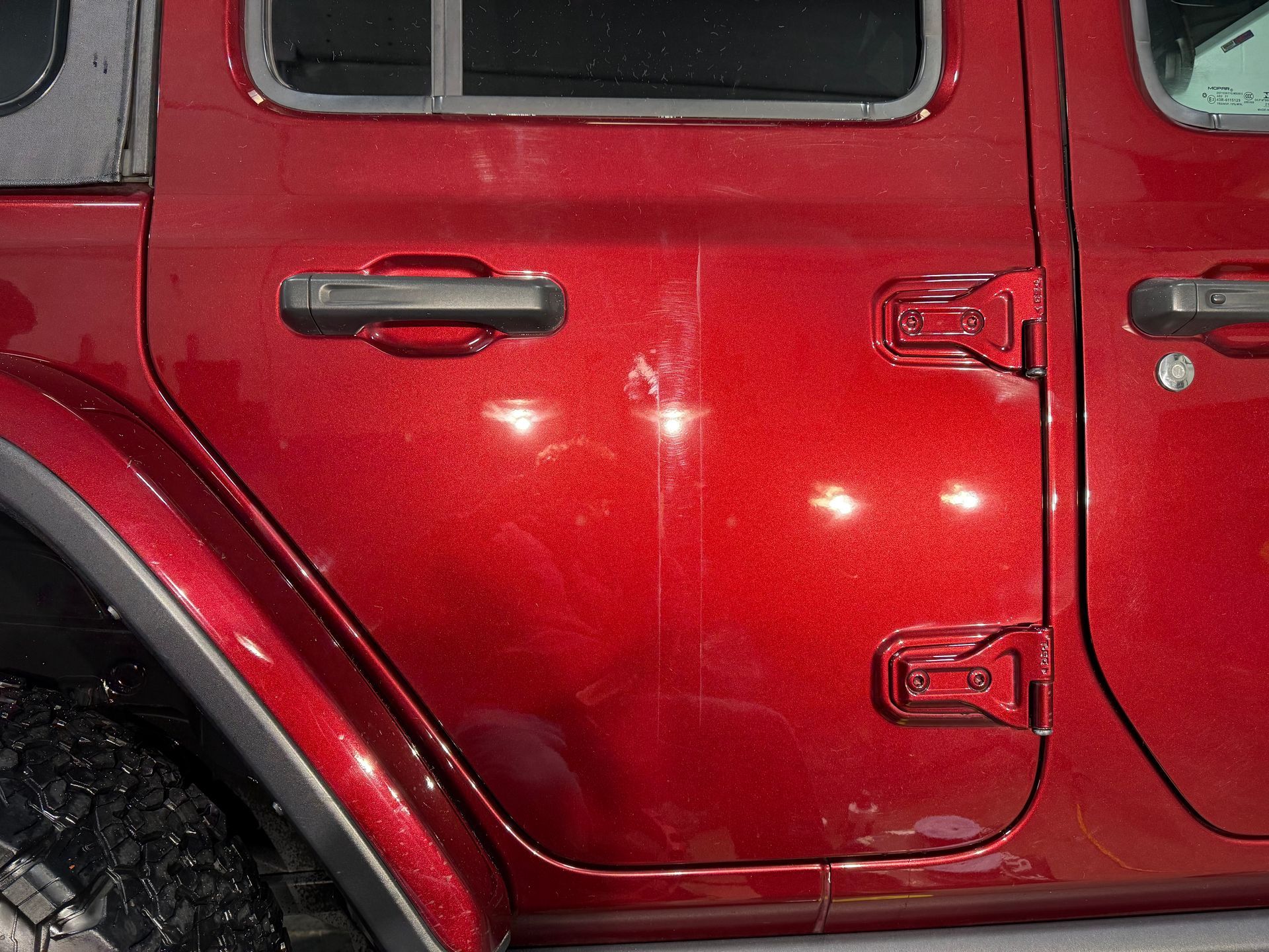 Red Jeep Wrangler door with scratches and reflections.