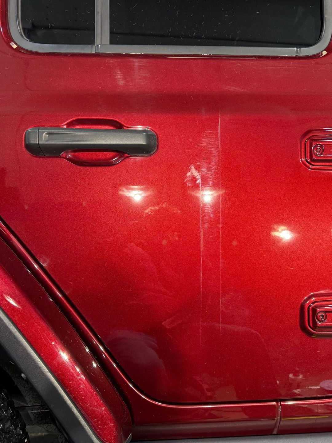Red car door with a black handle, showing reflections.
