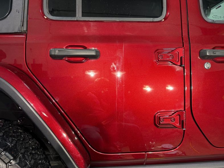 Red Jeep Wrangler door with scratches and reflections.