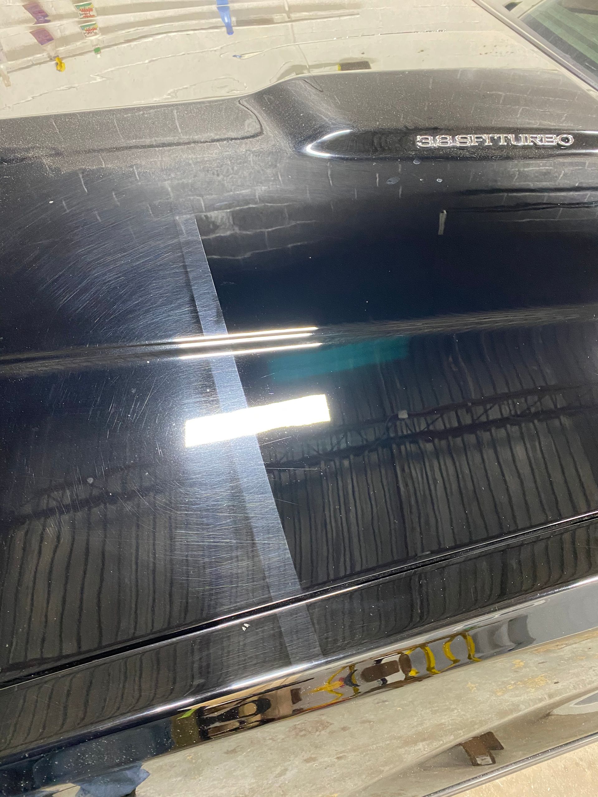 Black car door, half polished showing scratches, other half shiny, reflecting a bright light.