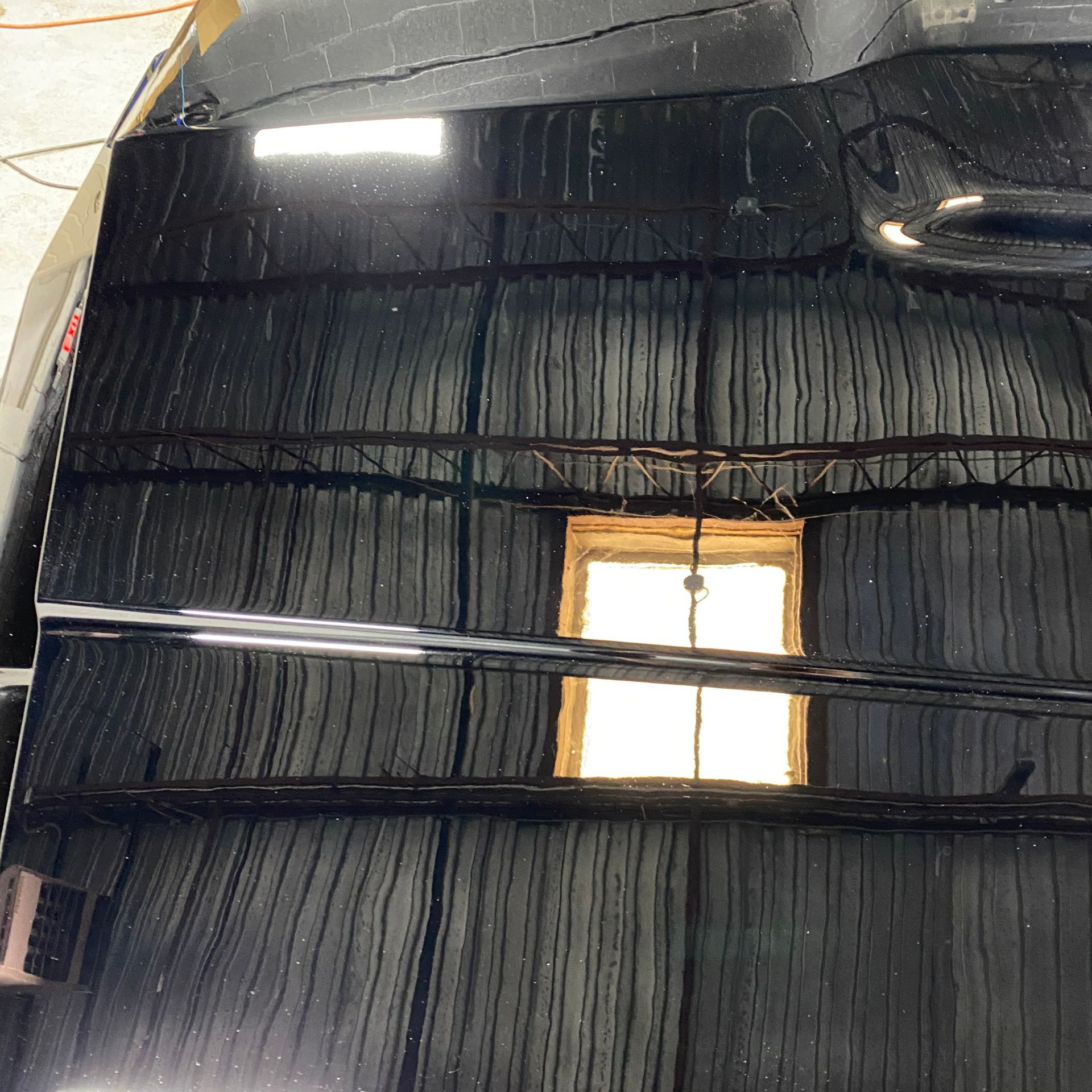 Black car hood reflecting an interior with exposed beams, a window, and lines.