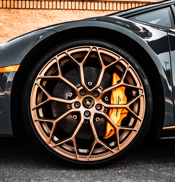 Close-up of a gray Lamborghini car wheel with bronze rims and orange brake calipers.