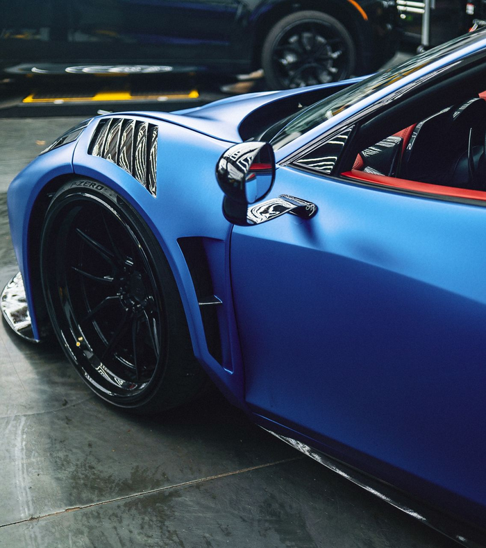 Blue sports car with black wheels and side vents, parked indoors.