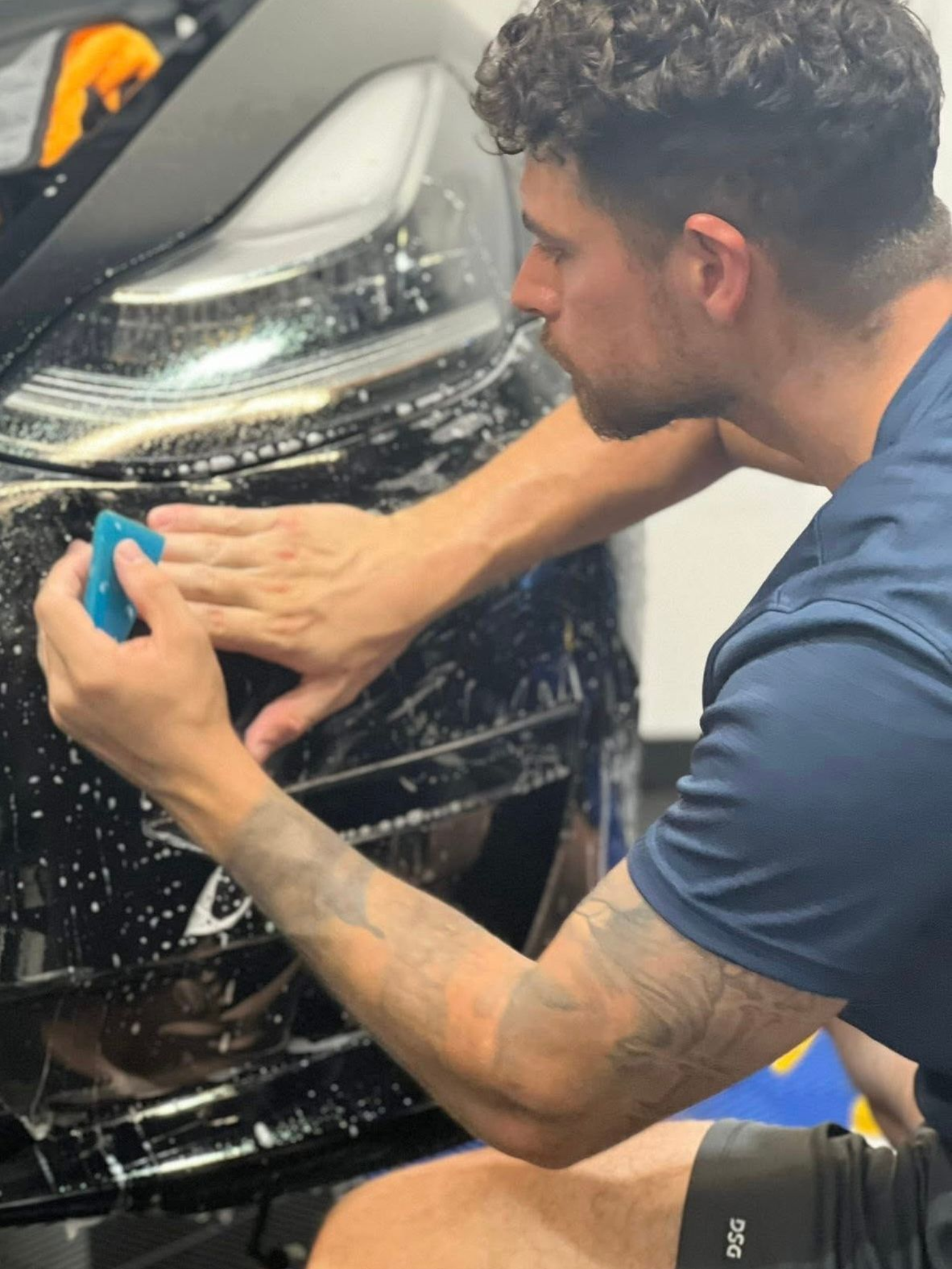 Man applying film to black car bumper, using a smoothing tool.